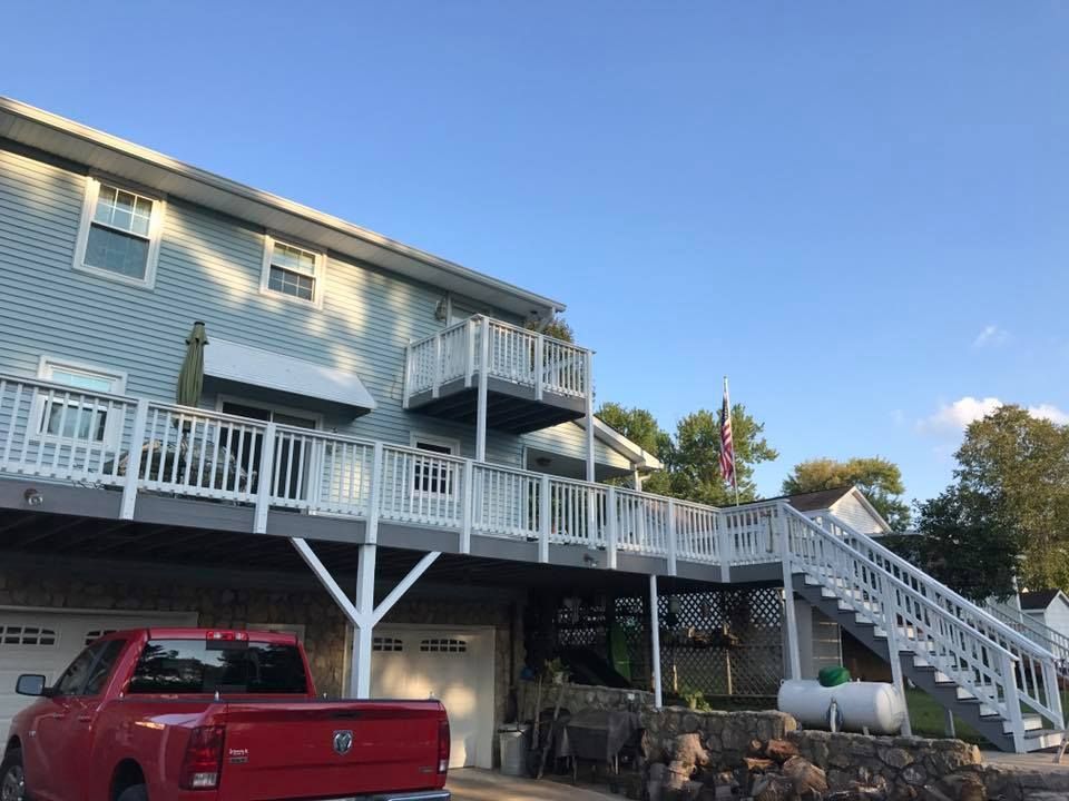 A red truck is parked in front of a house with a deck and stairs.