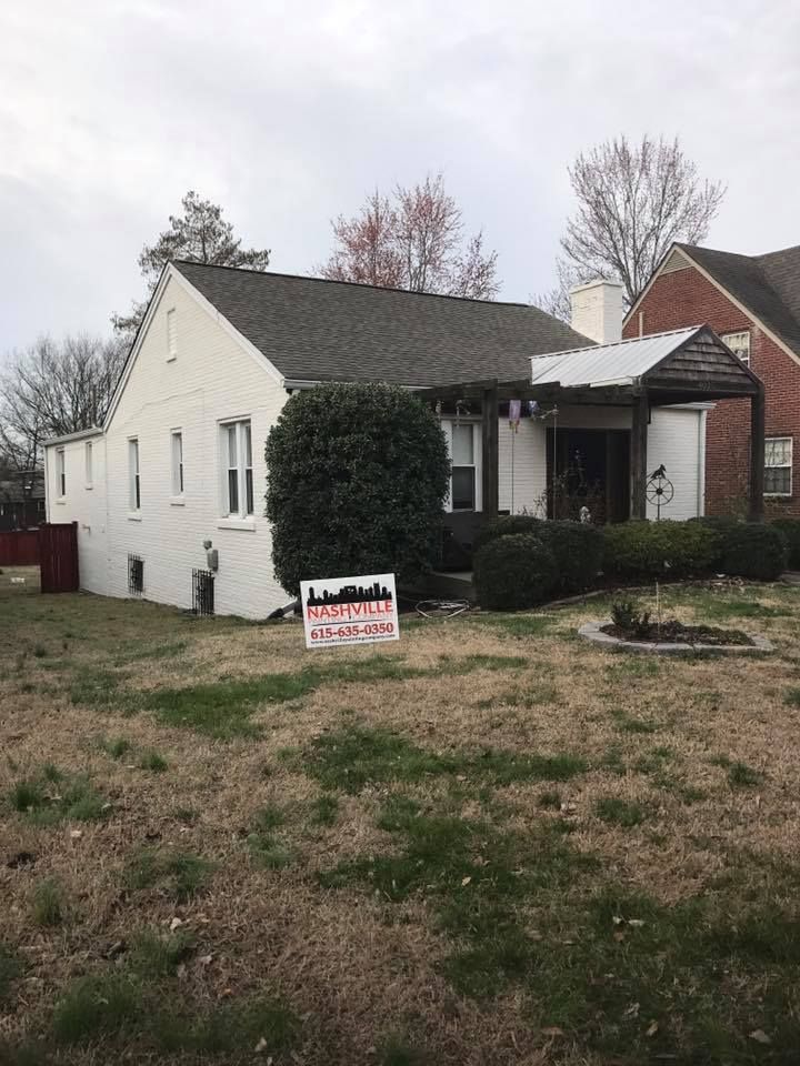 A white house with a gray roof and a sign in front of it.