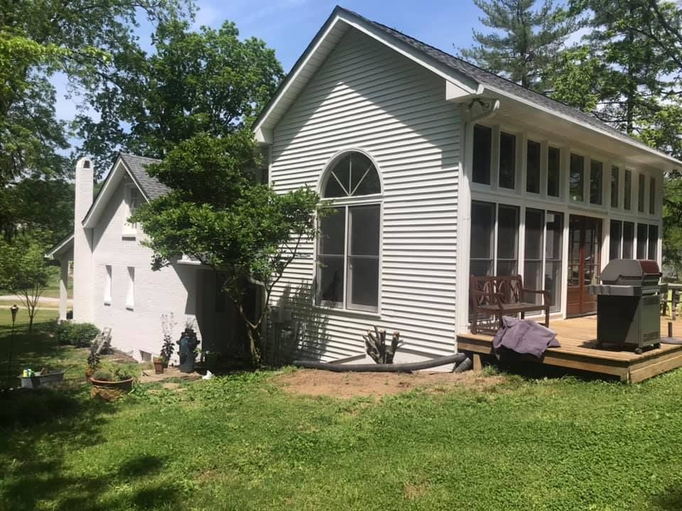 A white house with a screened in porch and a grill in the backyard.