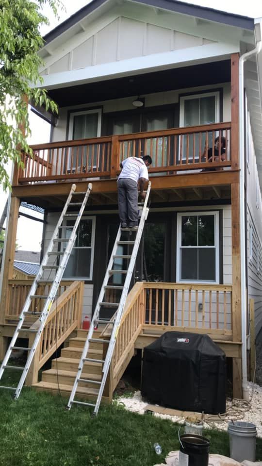 A man is standing on a ladder painting the deck of a house.