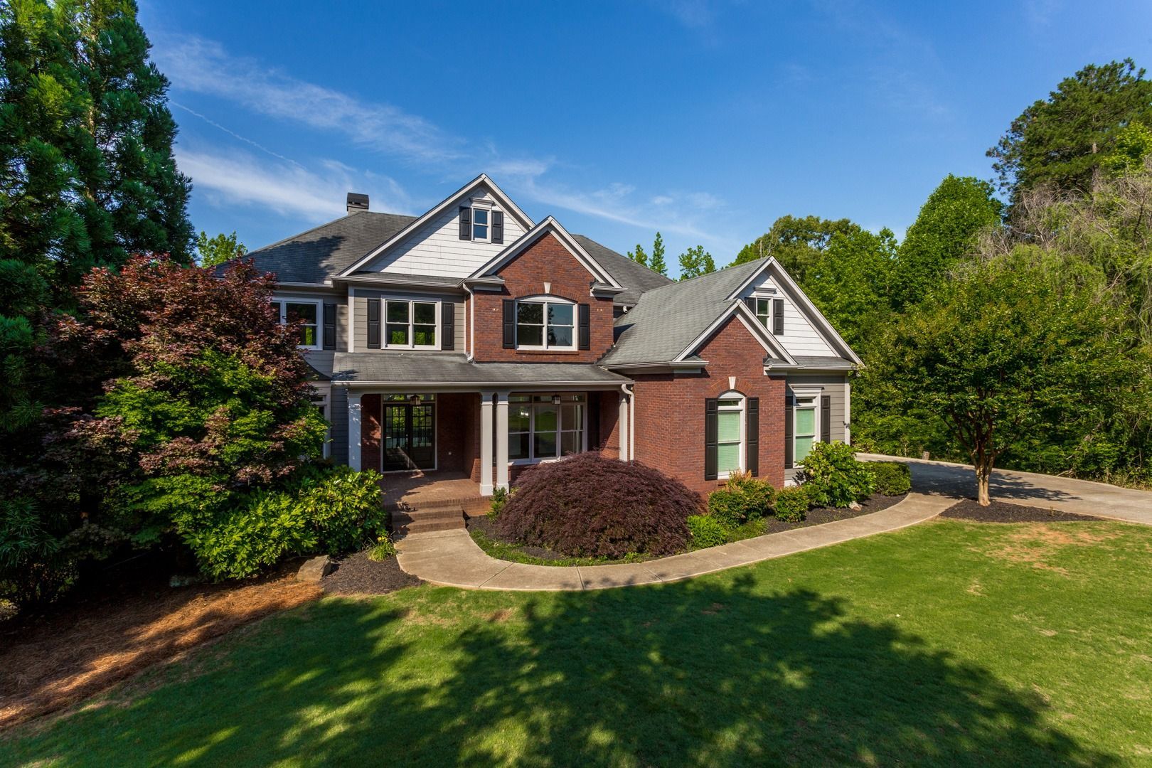 A large brick house with a large lawn in front of it surrounded by trees.