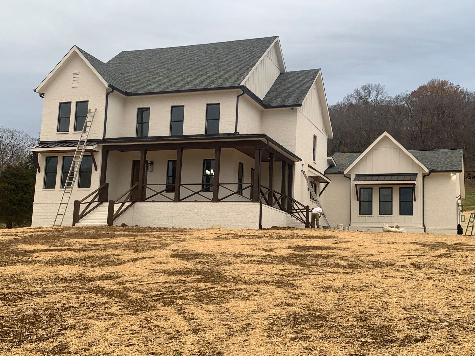 A large white house with a porch is sitting on top of a dirt field.