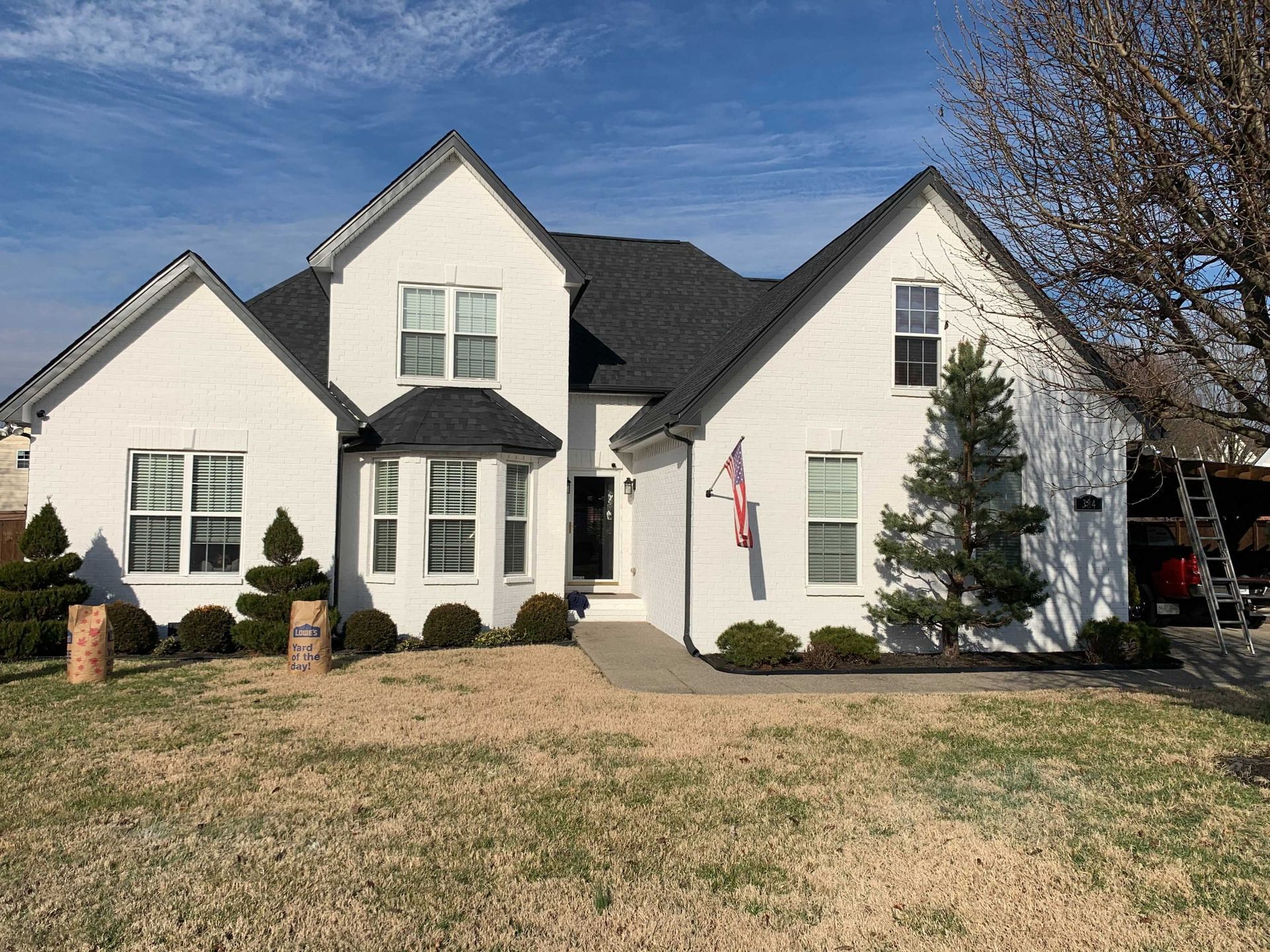 A large white house with a black roof and a ladder in front of it.