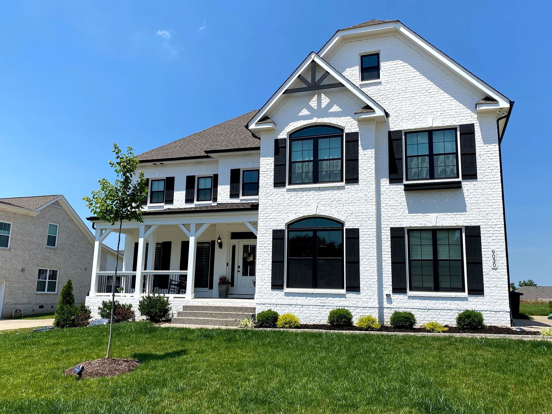 A large white house with black shutters is sitting on top of a lush green lawn.