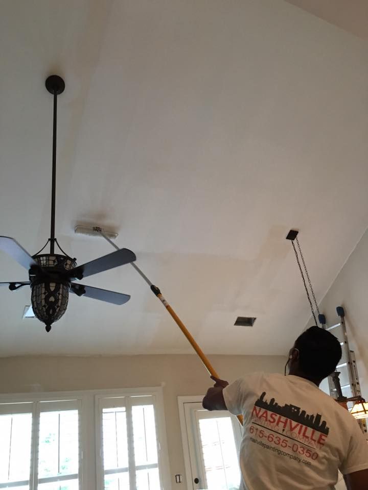 A man is painting the ceiling of a room with a brush.