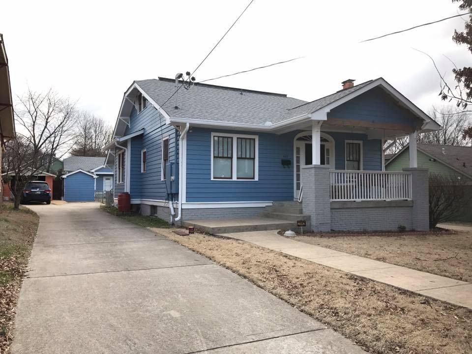 A blue house with a white porch and a car parked in front of it.