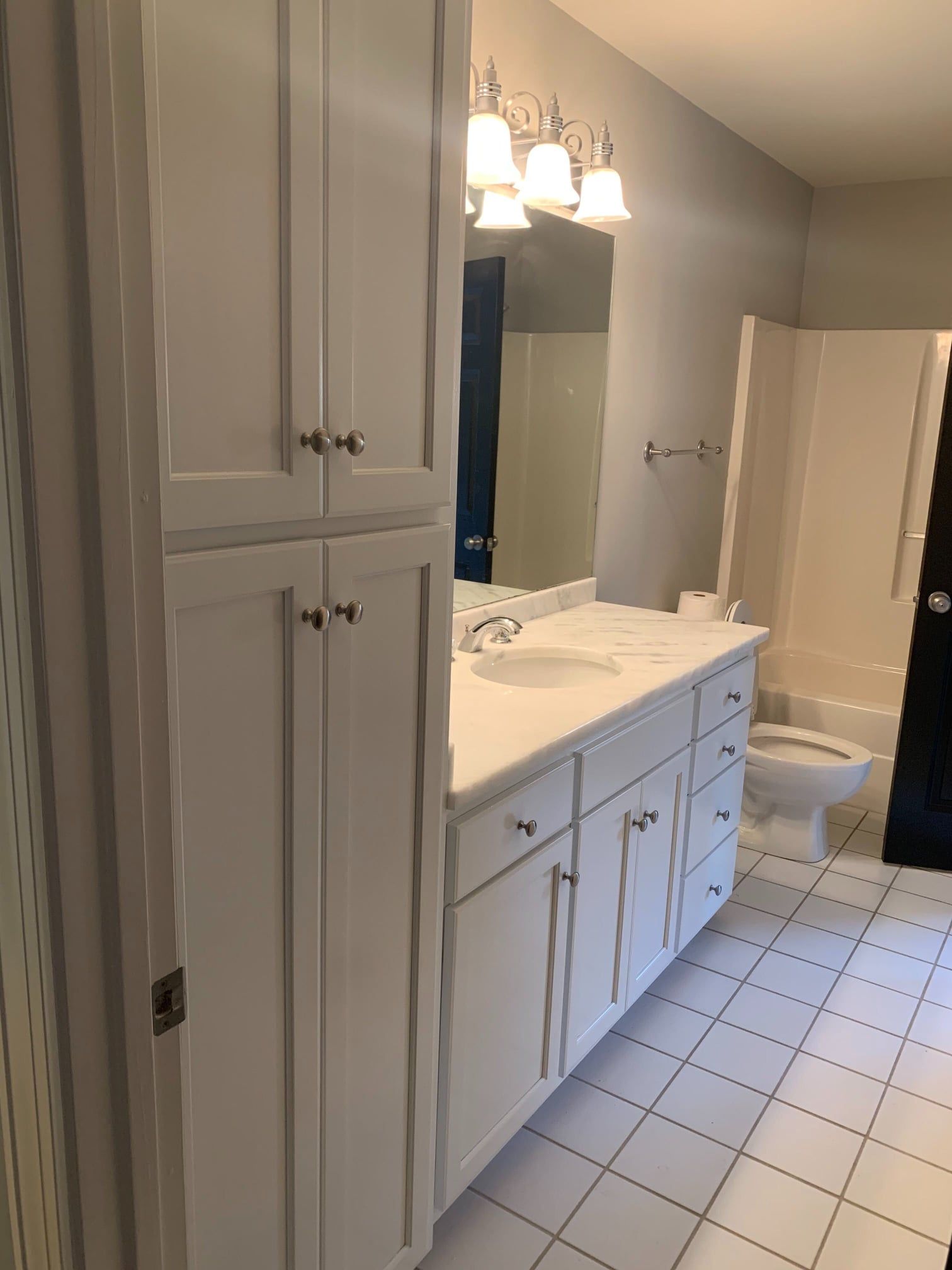 A bathroom with white cabinets , a sink , a toilet and a mirror.