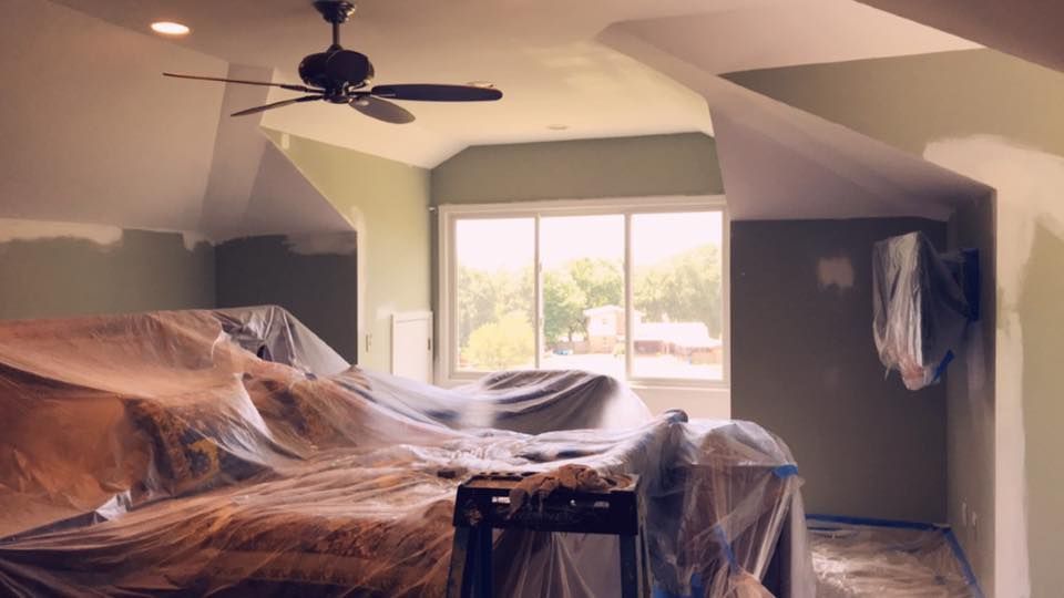 A living room with a ceiling fan and a couch covered in plastic.