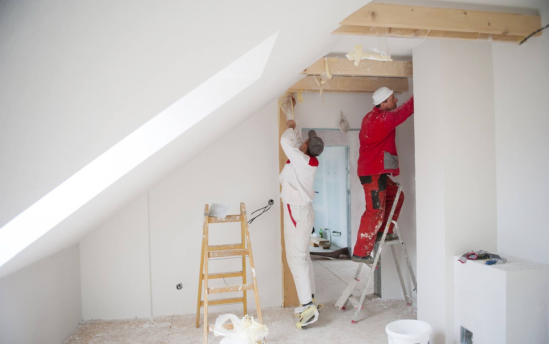 Two men are working on a wall in an attic.