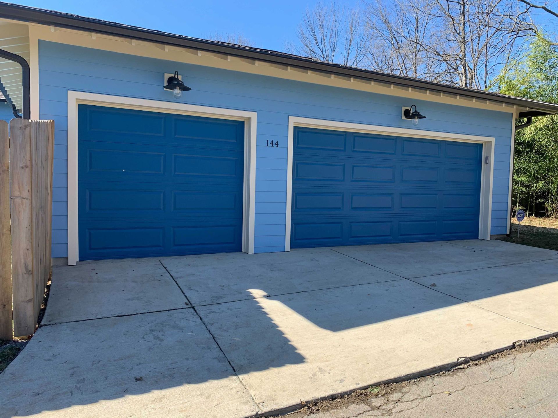 A blue garage with two blue garage doors and a wooden fence.