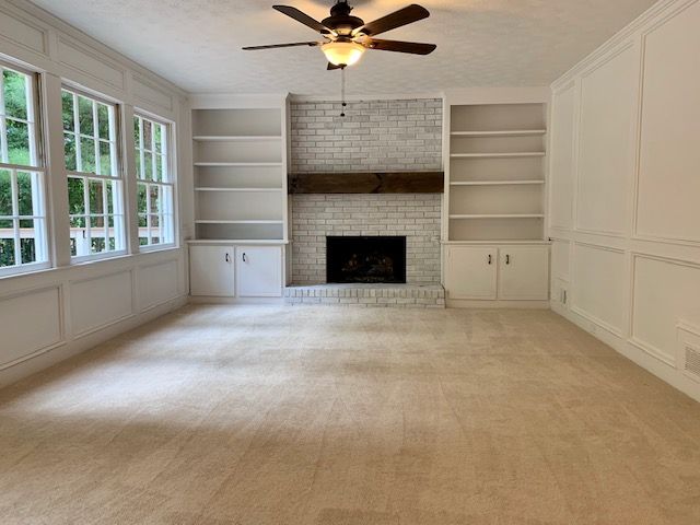 An empty living room with a fireplace and ceiling fan.