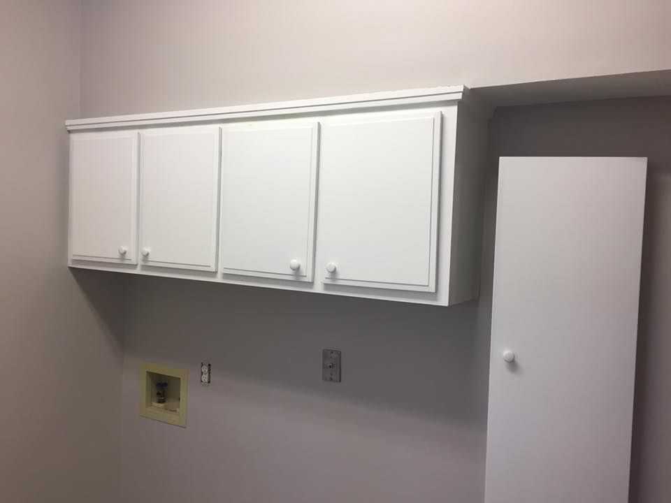 A laundry room with white cabinets and a door