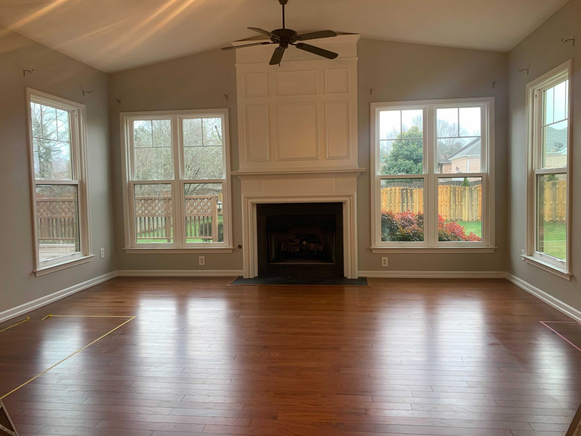 An empty living room with hardwood floors , a fireplace and a ceiling fan.