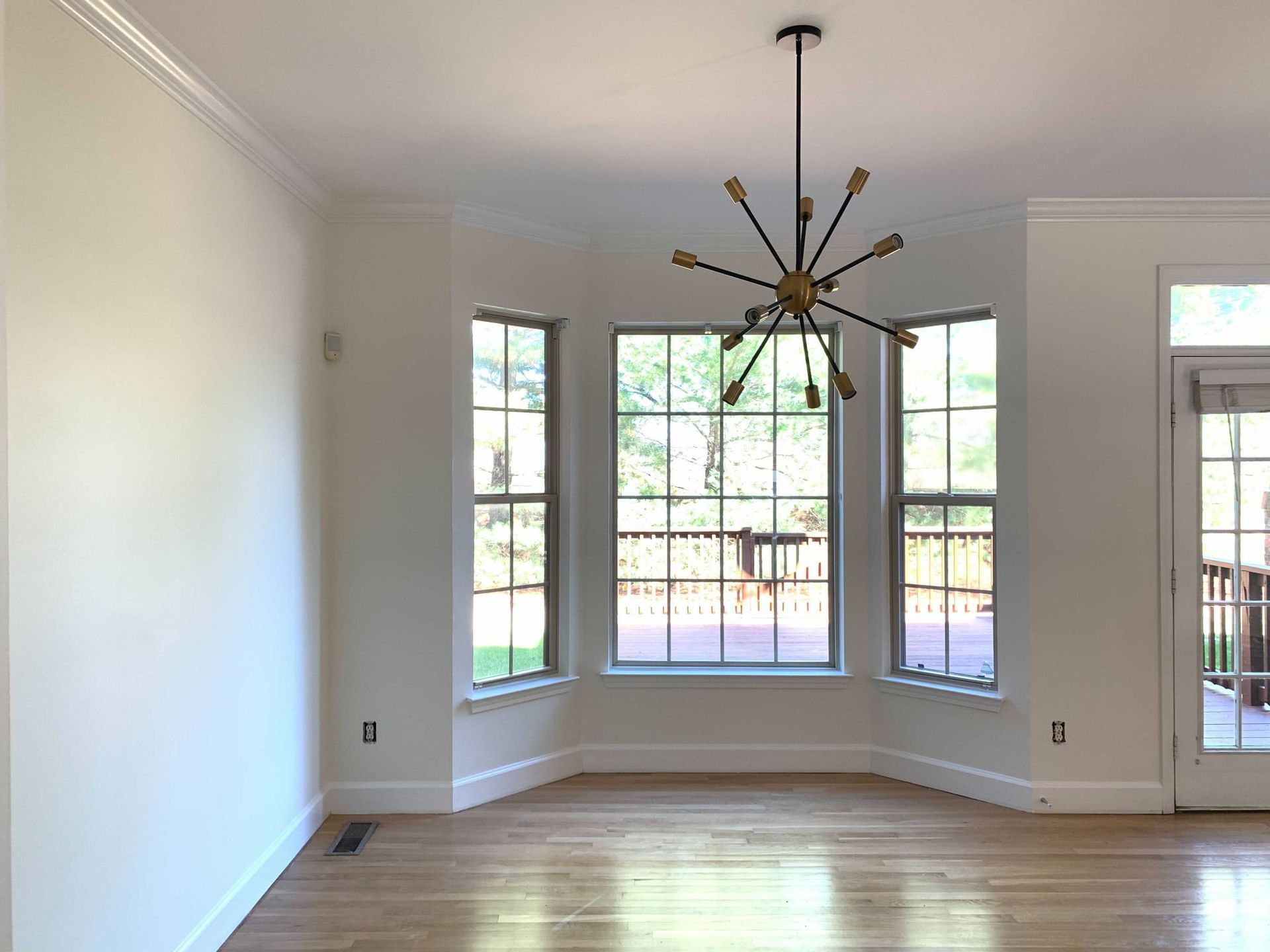 An empty living room with hardwood floors and a chandelier hanging from the ceiling.