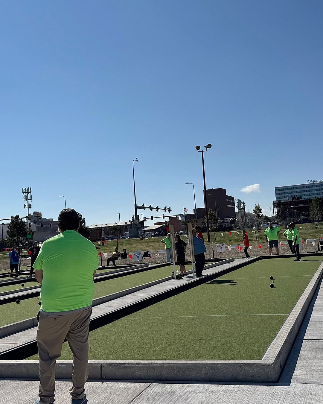 People playing bocce ball on a green turf court under a blue sky