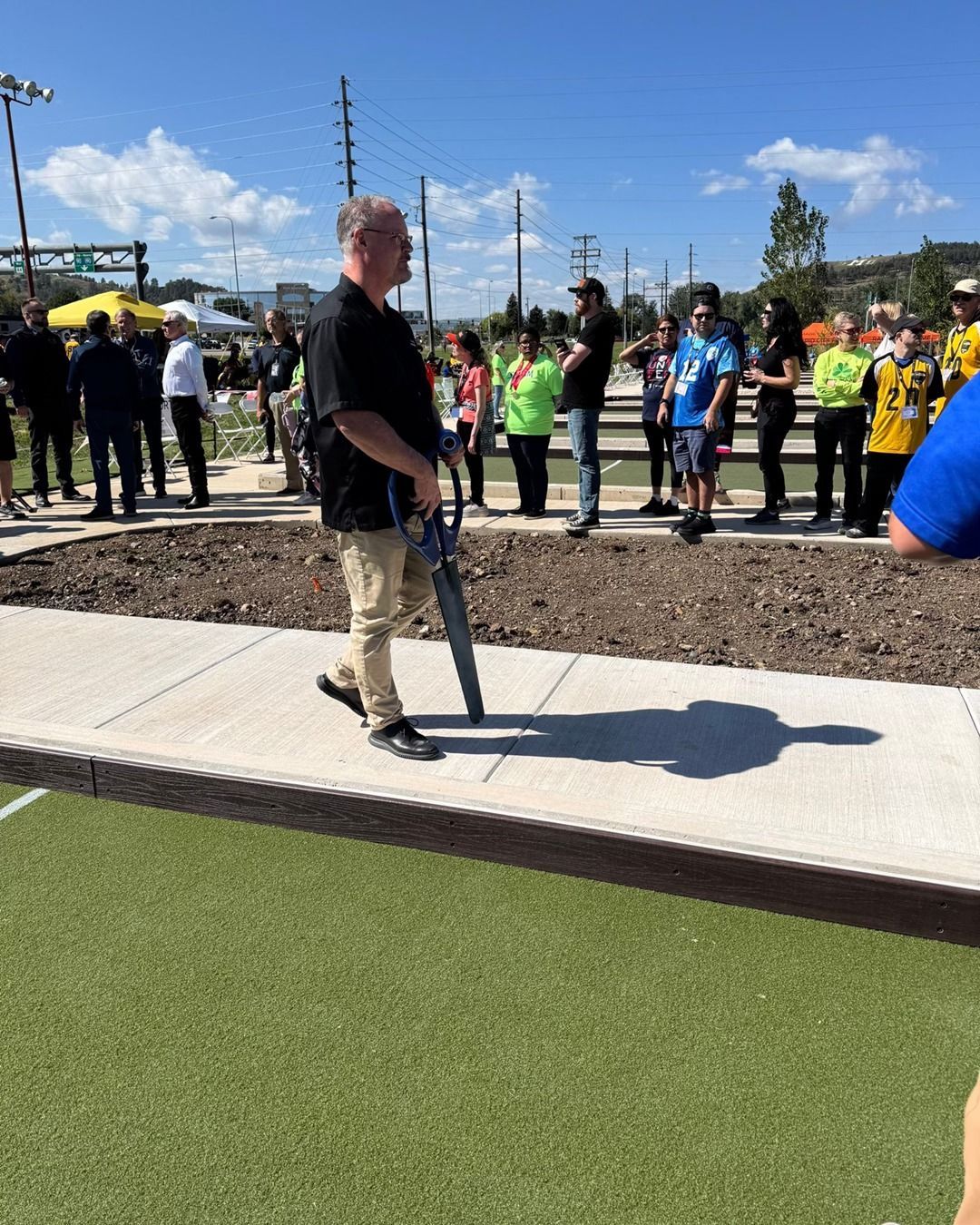 Man holding a chainsaw stands on a sidewalk at an outdoor event with a crowd of people in the background