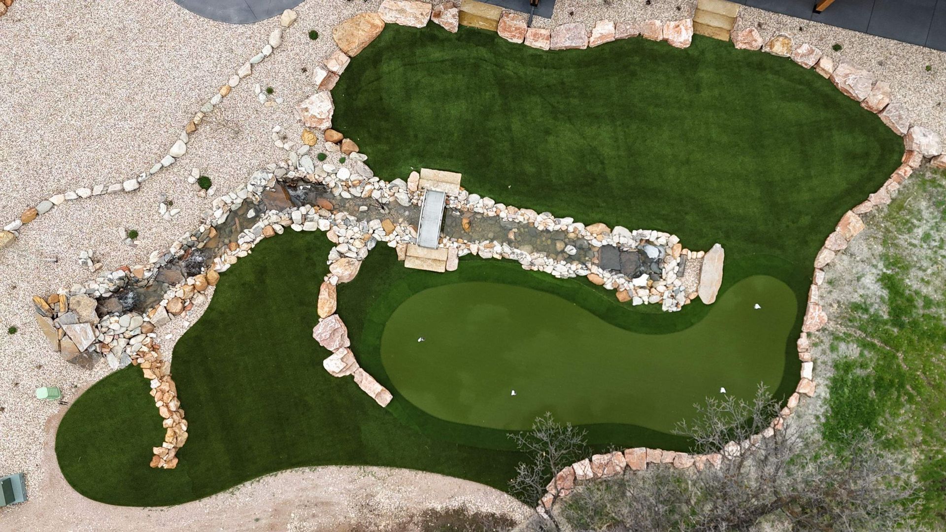 Overhead view of a small putting green, stream, and decorative rocks
