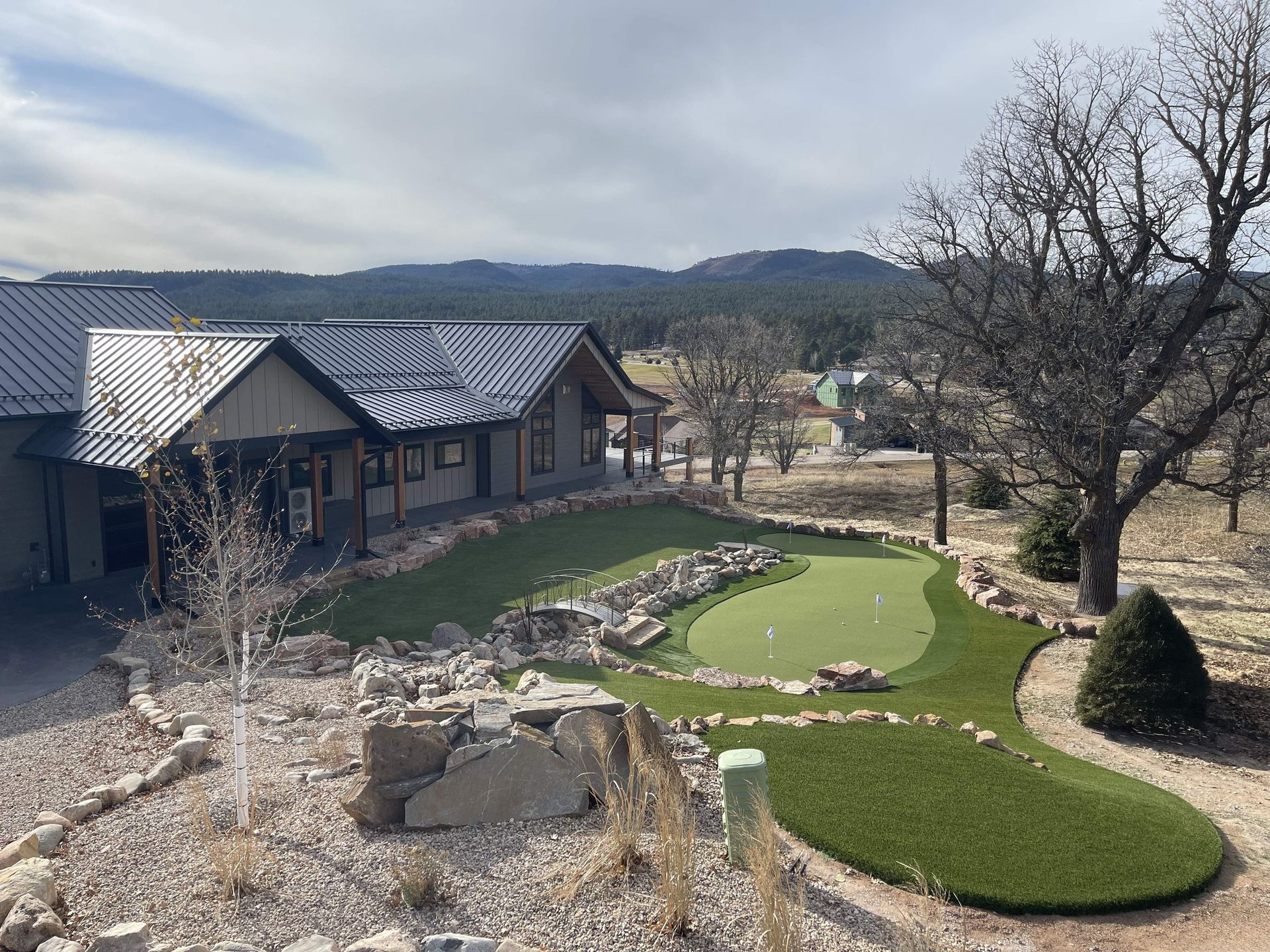House with putting green, rocky landscaping, and mountain view under cloudy sky