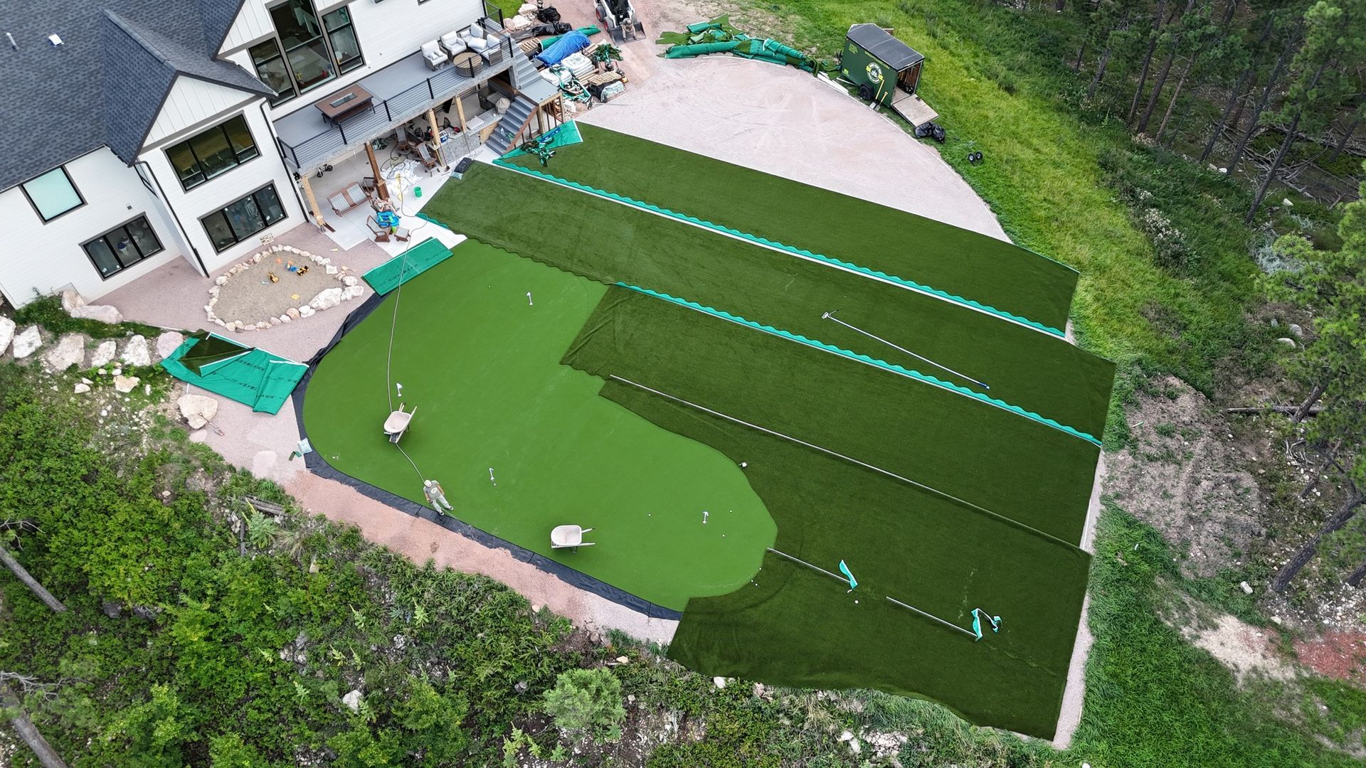 Aerial view of a backyard putting green with multiple sections and a home in the background