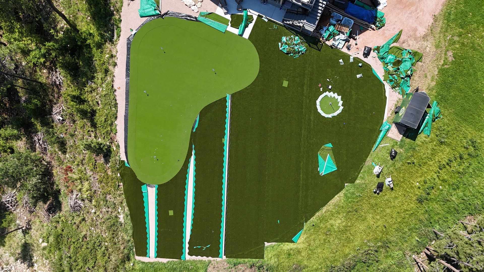 Aerial view of a partially constructed putting green with green artificial turf, surrounded by natural grass and a path