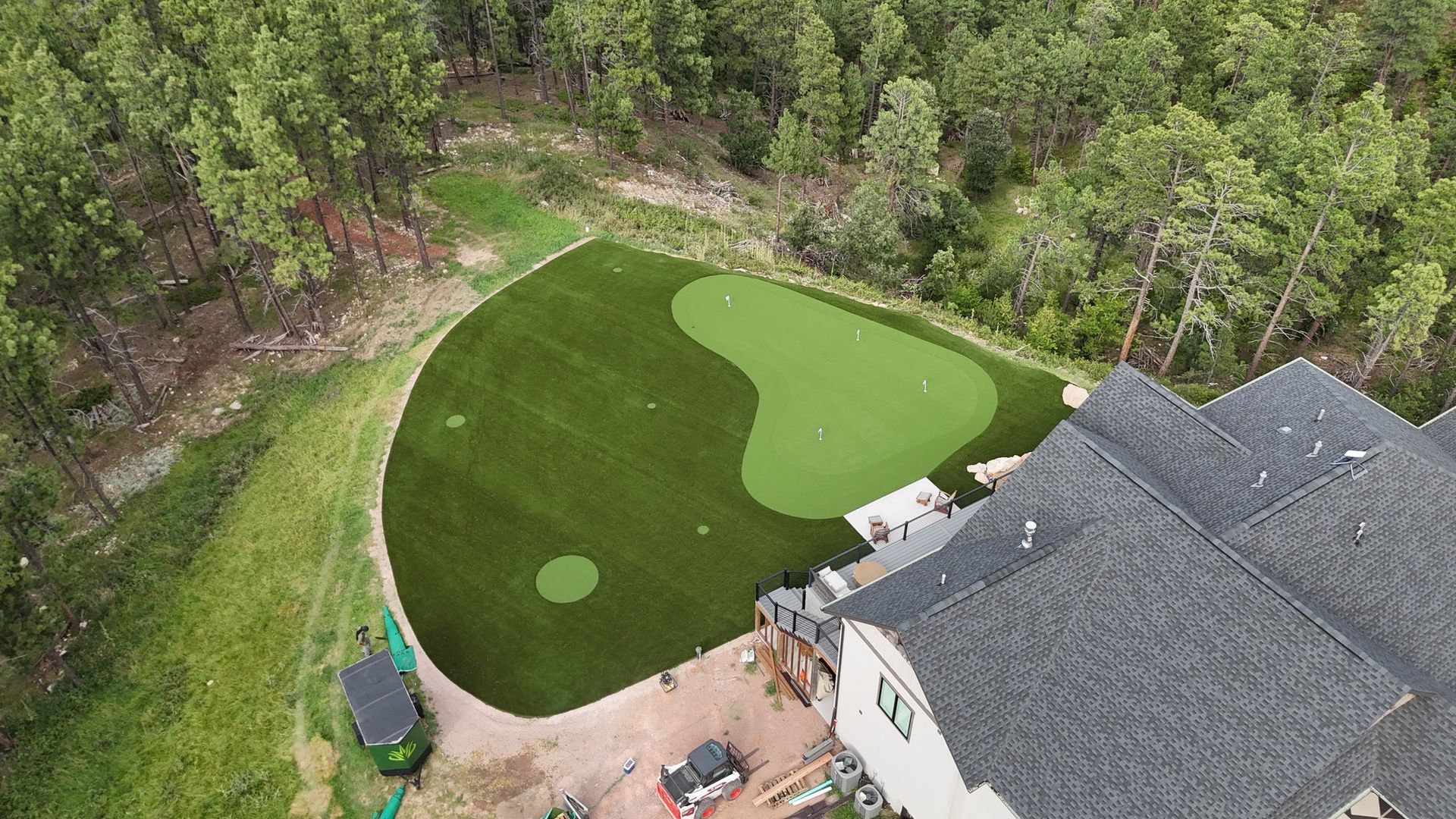 Aerial view of a custom putting green next to a house, surrounded by trees