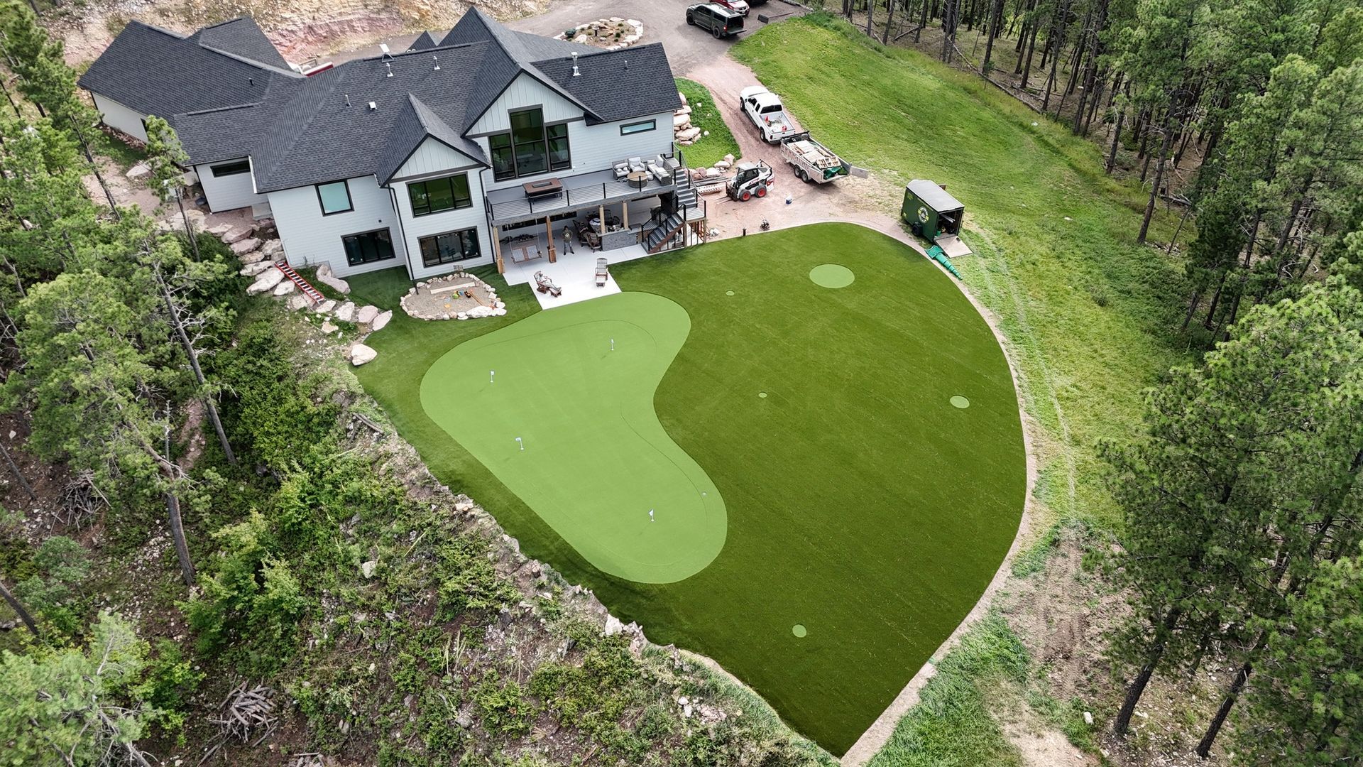 Aerial view of a large white house with a putting green in the backyard, surrounded by trees