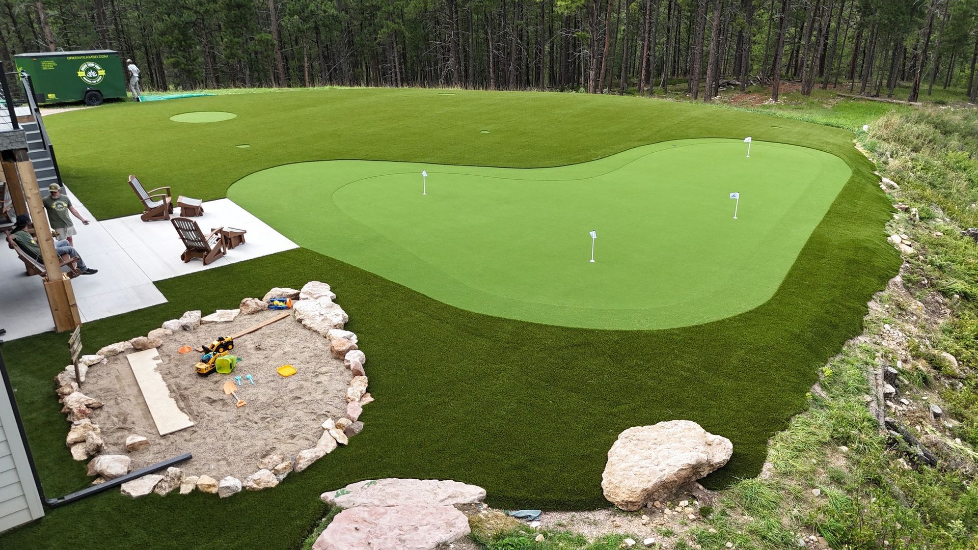 Backyard putting green, with sand trap, next to a house and forest