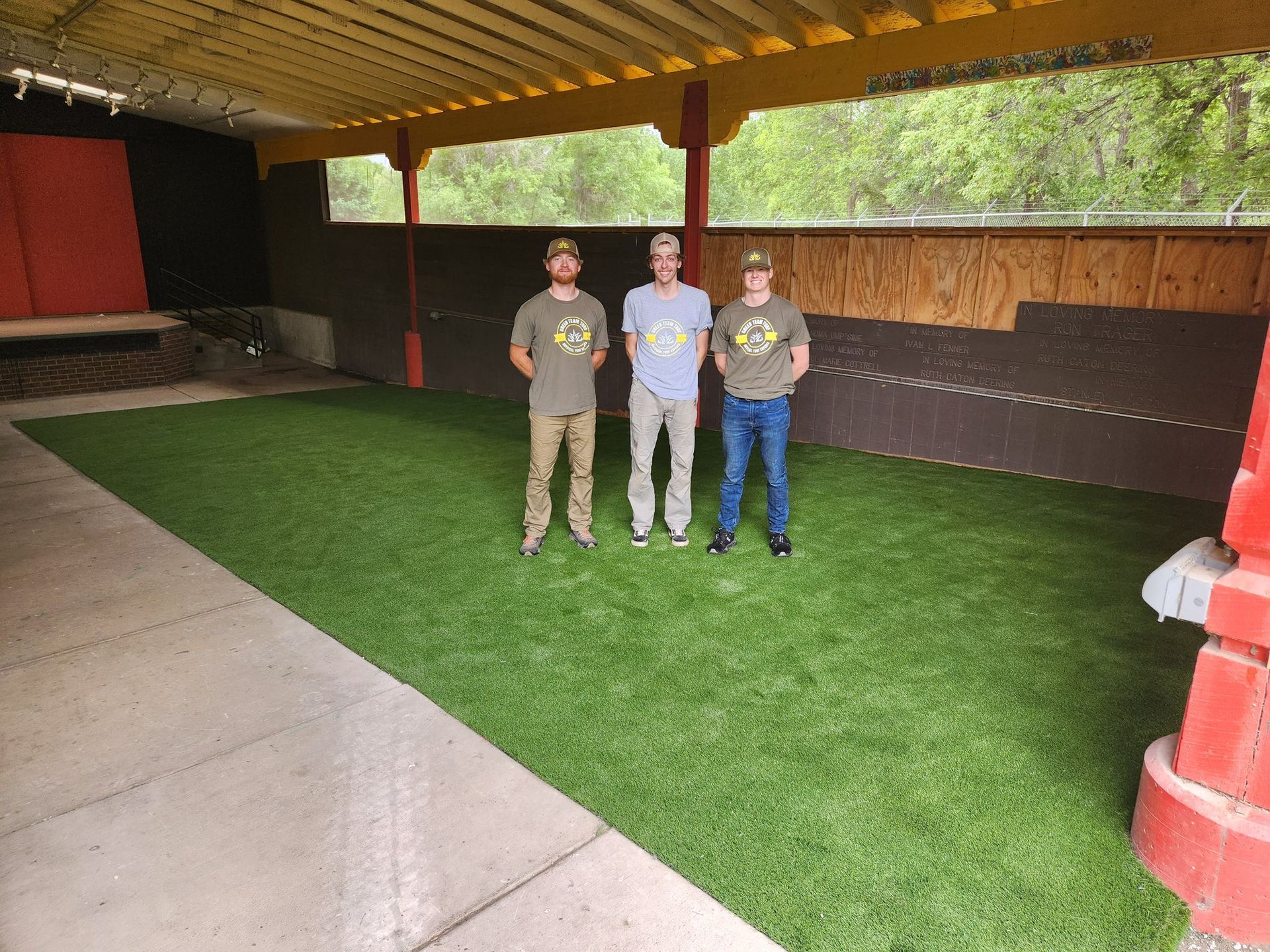 Three men standing on artificial turf under a yellow awning