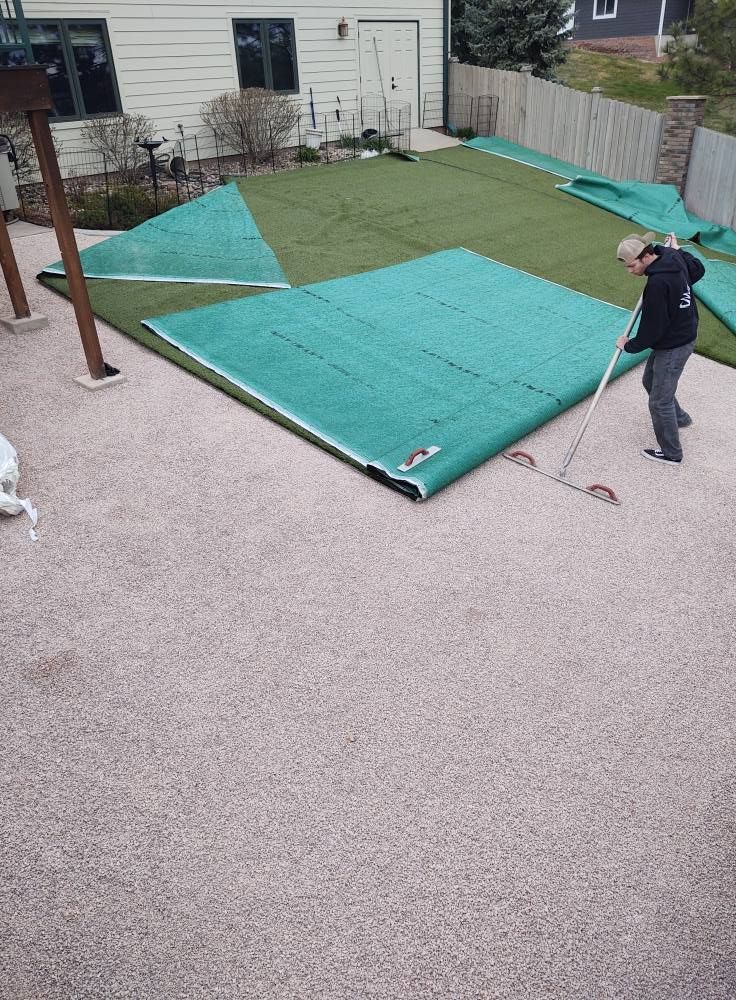 Person raking artificial turf on a gravel patio
