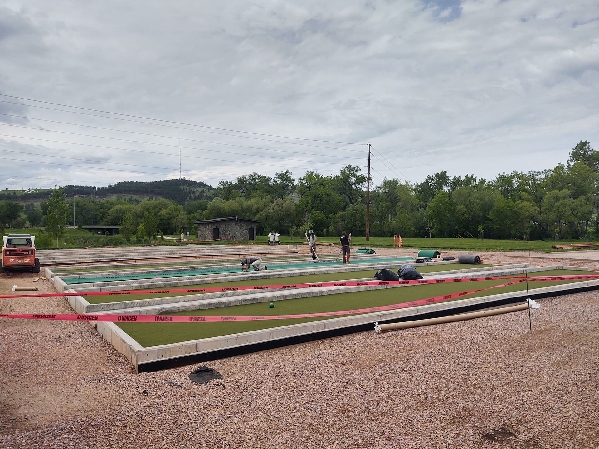 Construction site with workers, green turf, red caution tape, and a cloudy sky