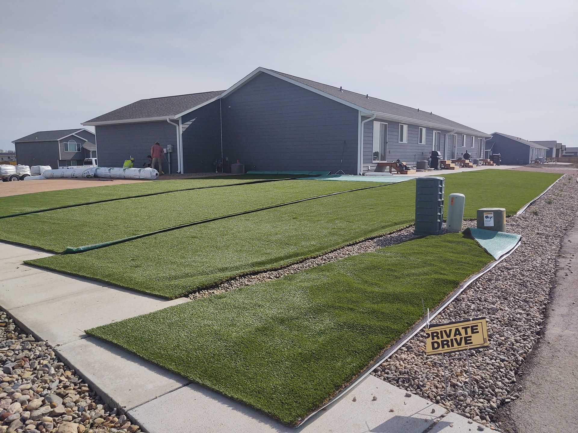 A row of new houses with green turf lawns, grey siding, and a 