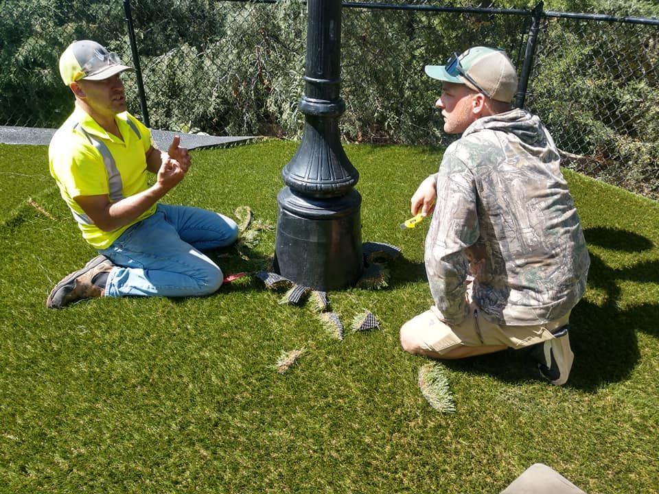 Two men sitting on artificial turf discussing something near a black lamppost