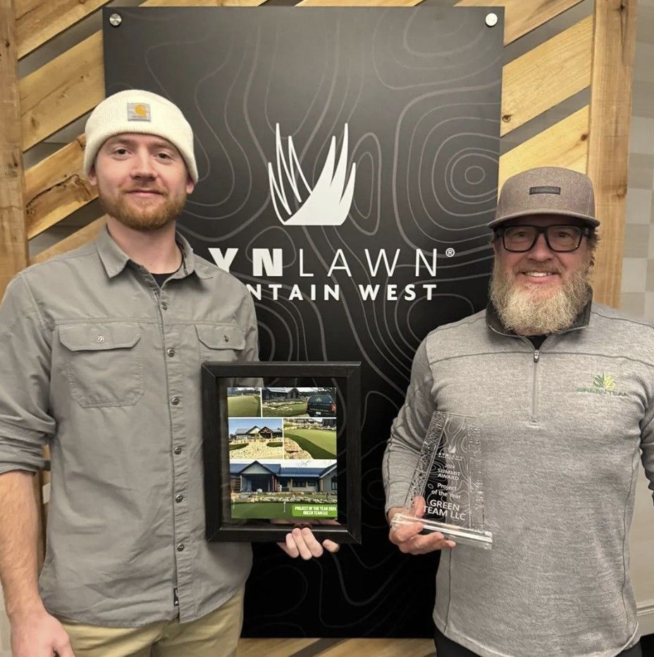 Two men holding a framed photo and an award, standing in front of a company sign
