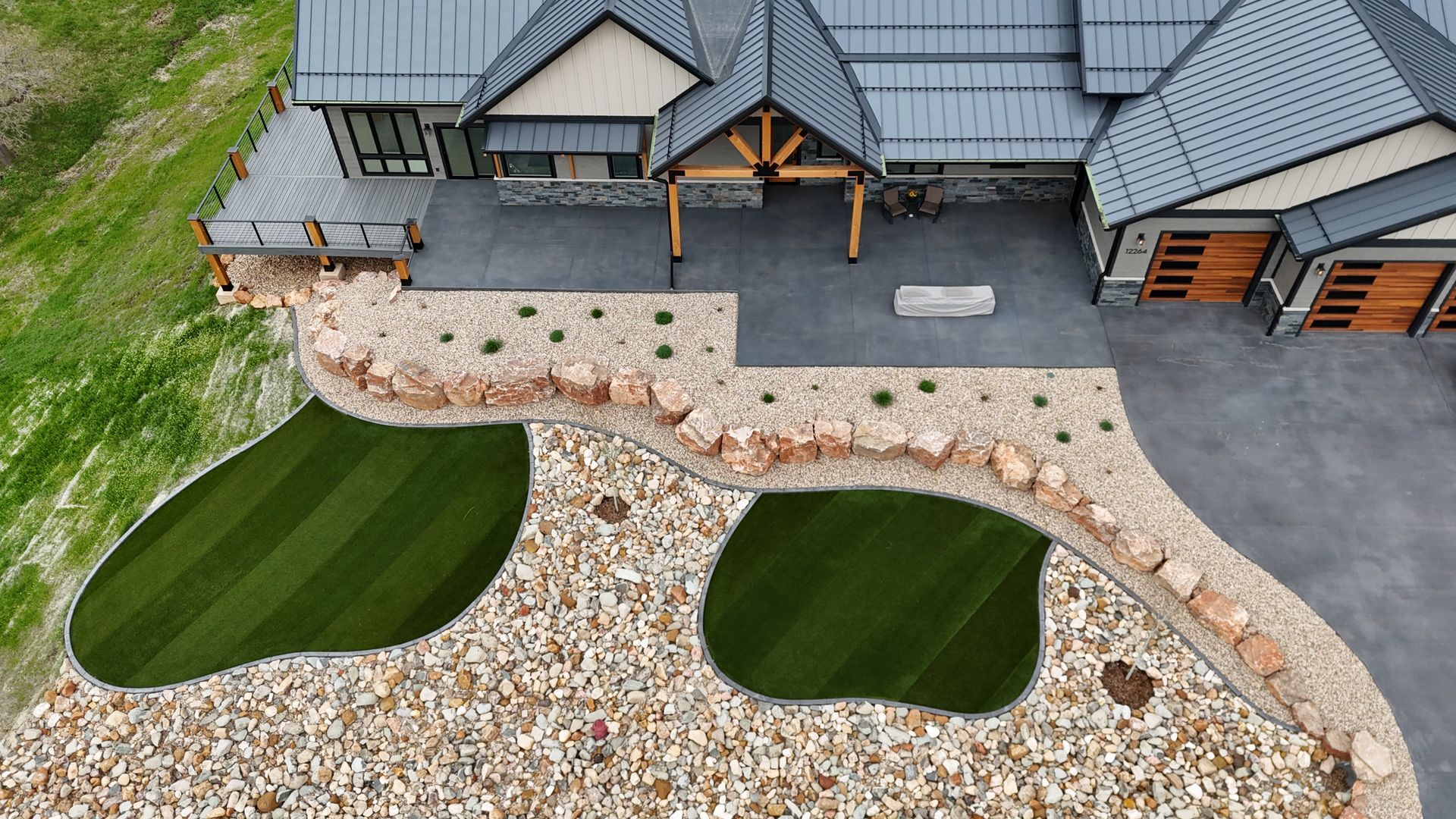Aerial view of a modern house with a rock garden, green grass patches, and concrete driveway.