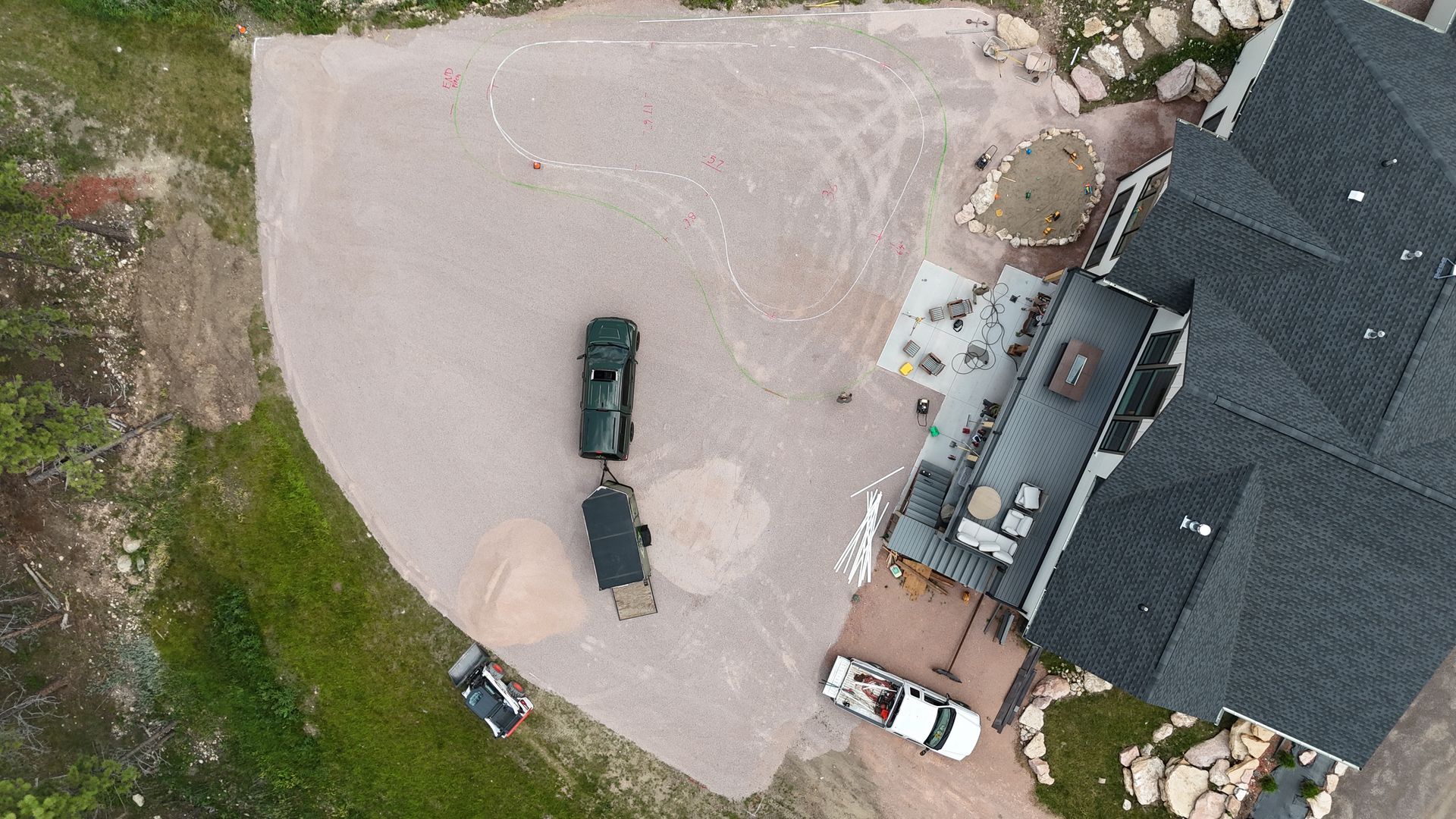 Overhead view of a house with trucks, trailers, and a gravel driveway. Green truck pulling a trailer.