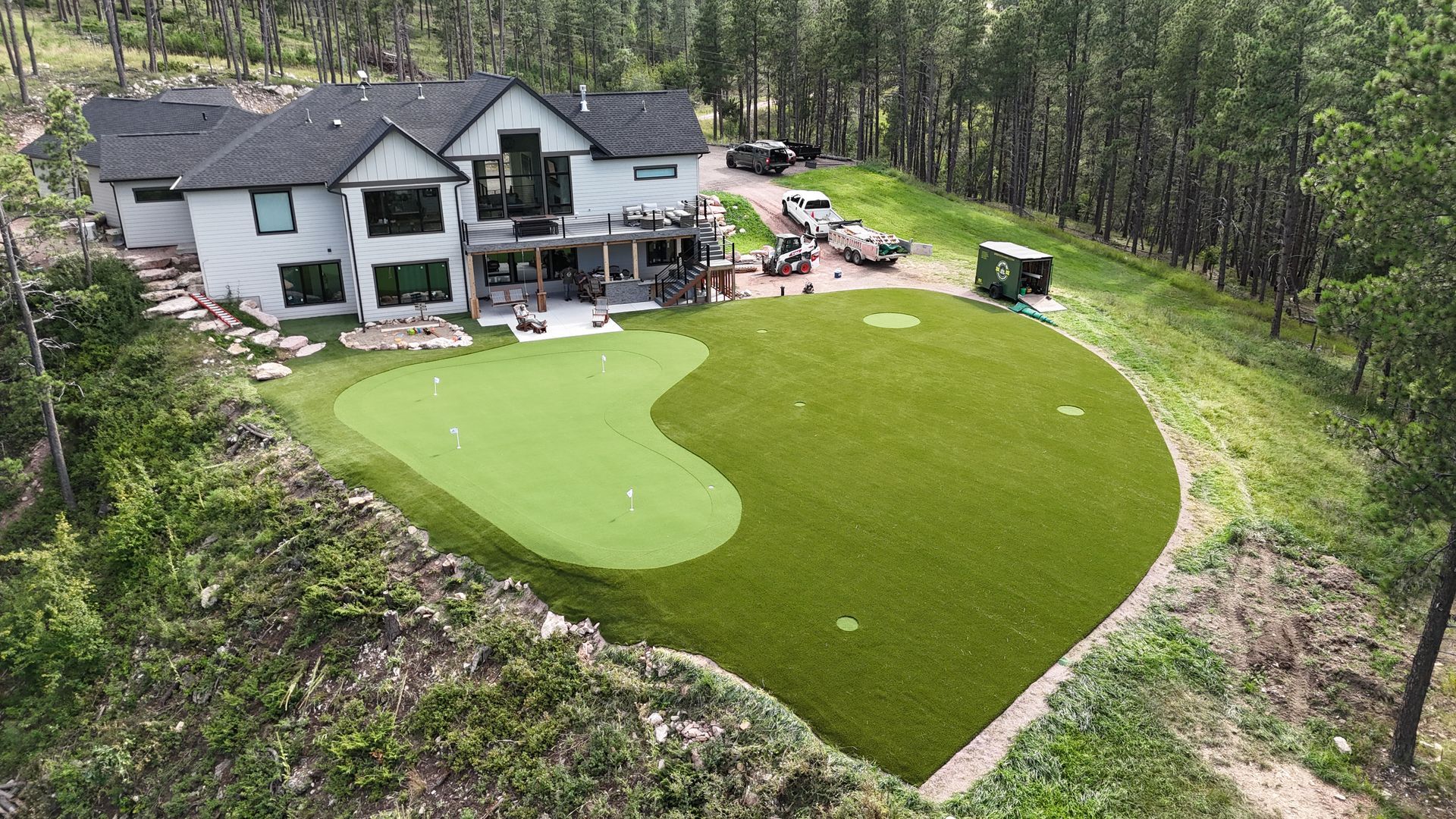 A modern house with a green artificial turf putting green on a sloped yard.