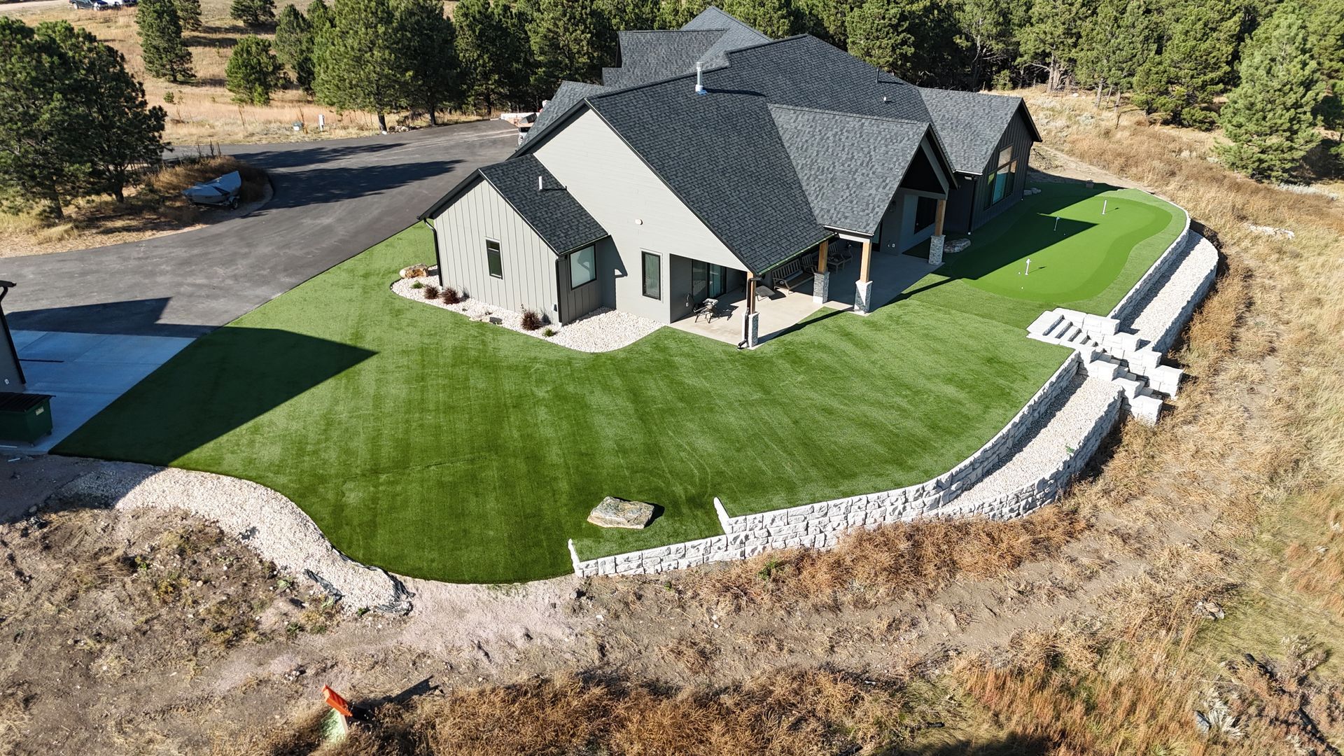 Aerial view of a modern house with a green lawn and stone retaining walls on a hillside.