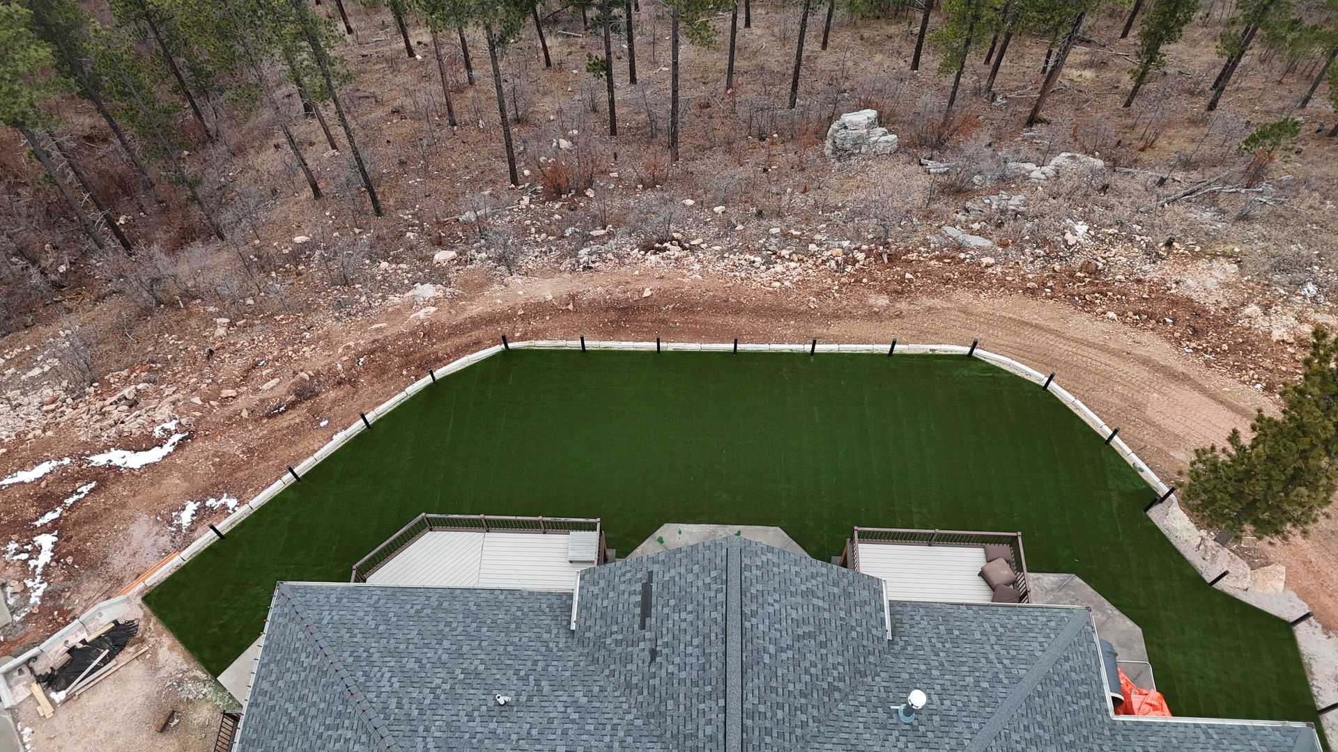 Aerial view of house with green lawn, driveway, and forest backdrop.
