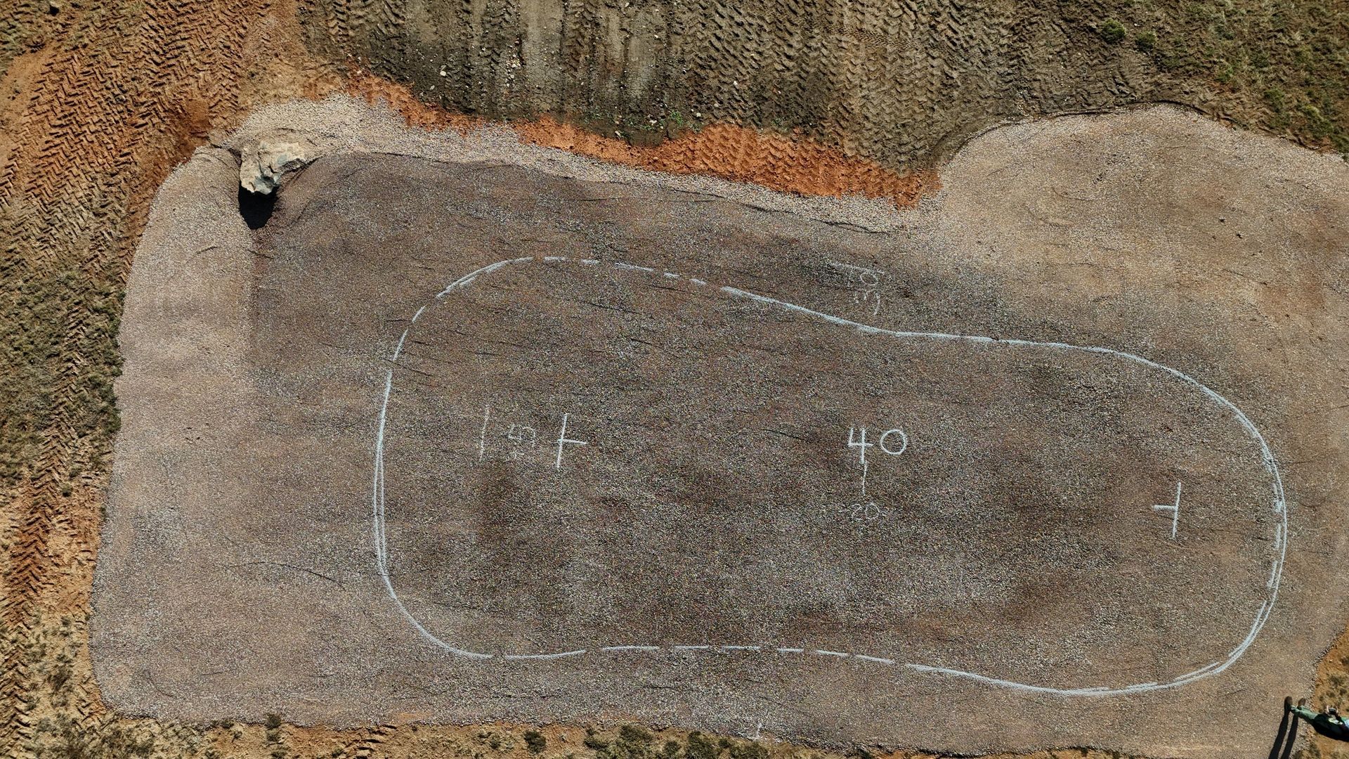 Aerial view of a brown, irregularly shaped area with a white outline. Some markings inside.