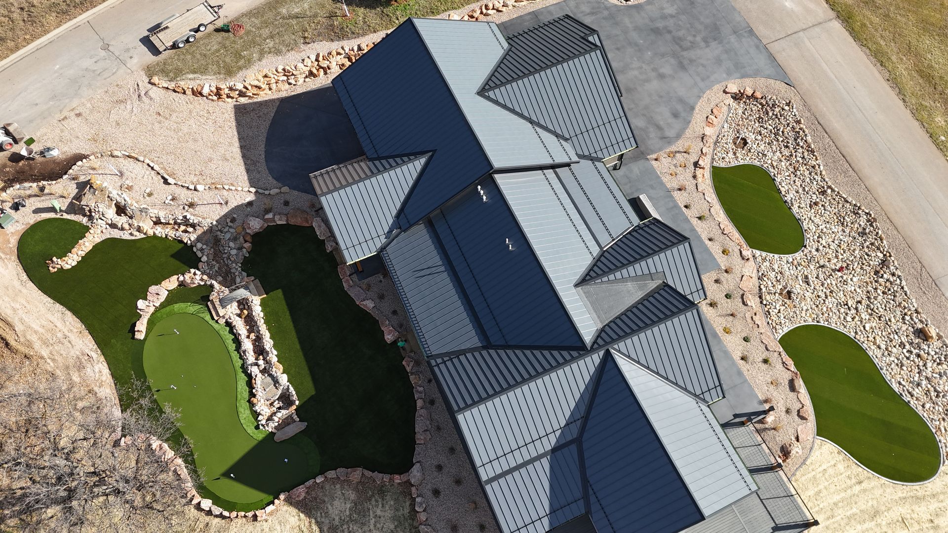 Overhead view of house with gray roof, putting green, and landscaped yard.