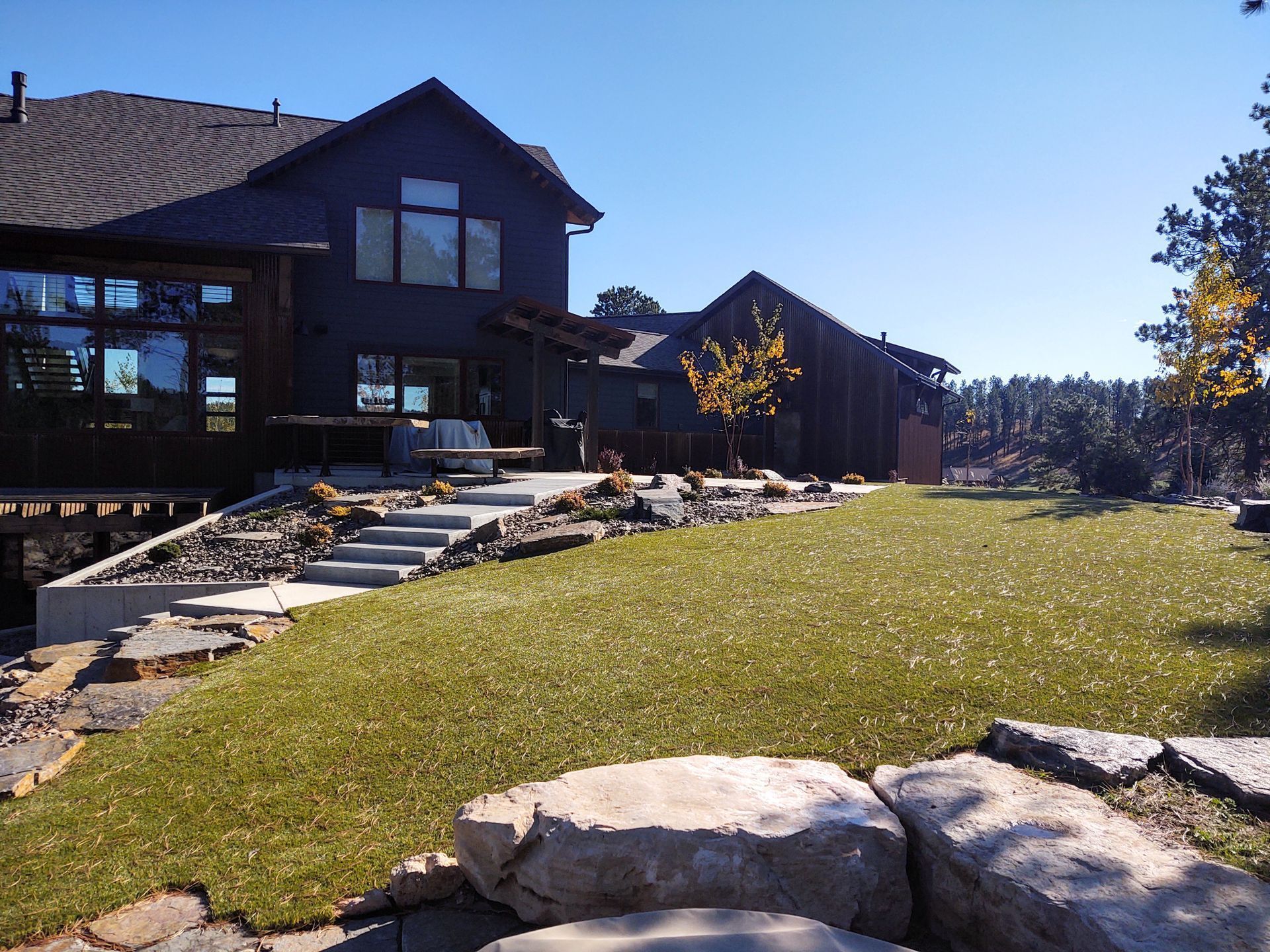 Dark-colored house with large windows, stone steps, and a grassy yard.