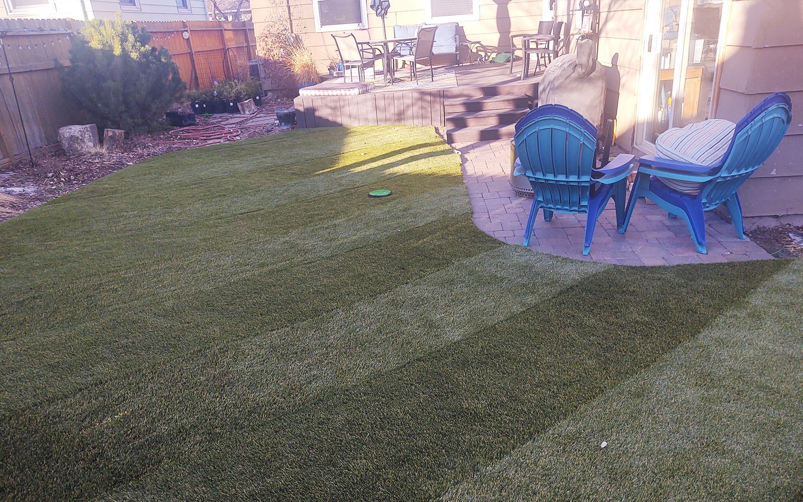 Backyard with green turf, blue chairs, and stone patio.