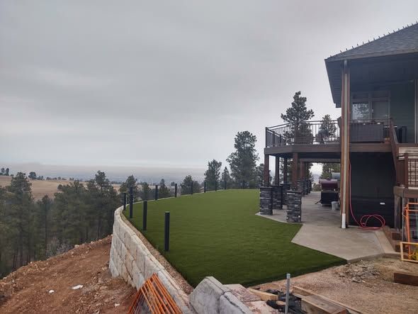 House with a green lawn, retaining wall, and overcast sky in a hillside setting
