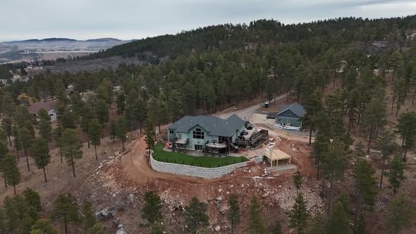 House nestled in a forested hillside, with a smaller building beside it and gravel pathways