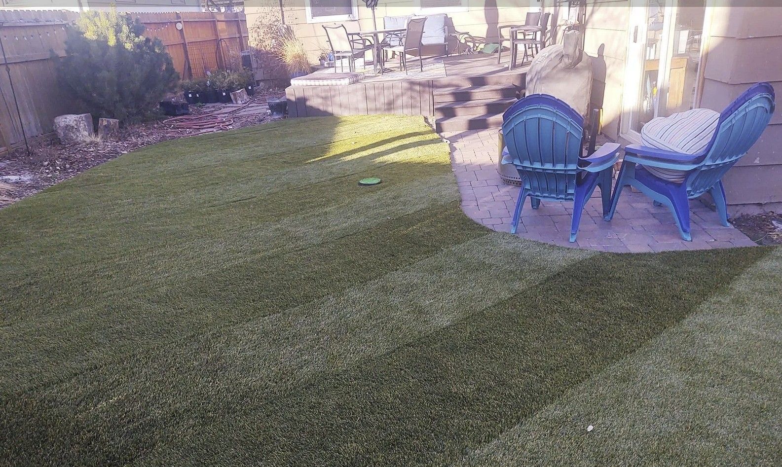 Backyard with artificial turf, two blue chairs, patio, and a wooden fence