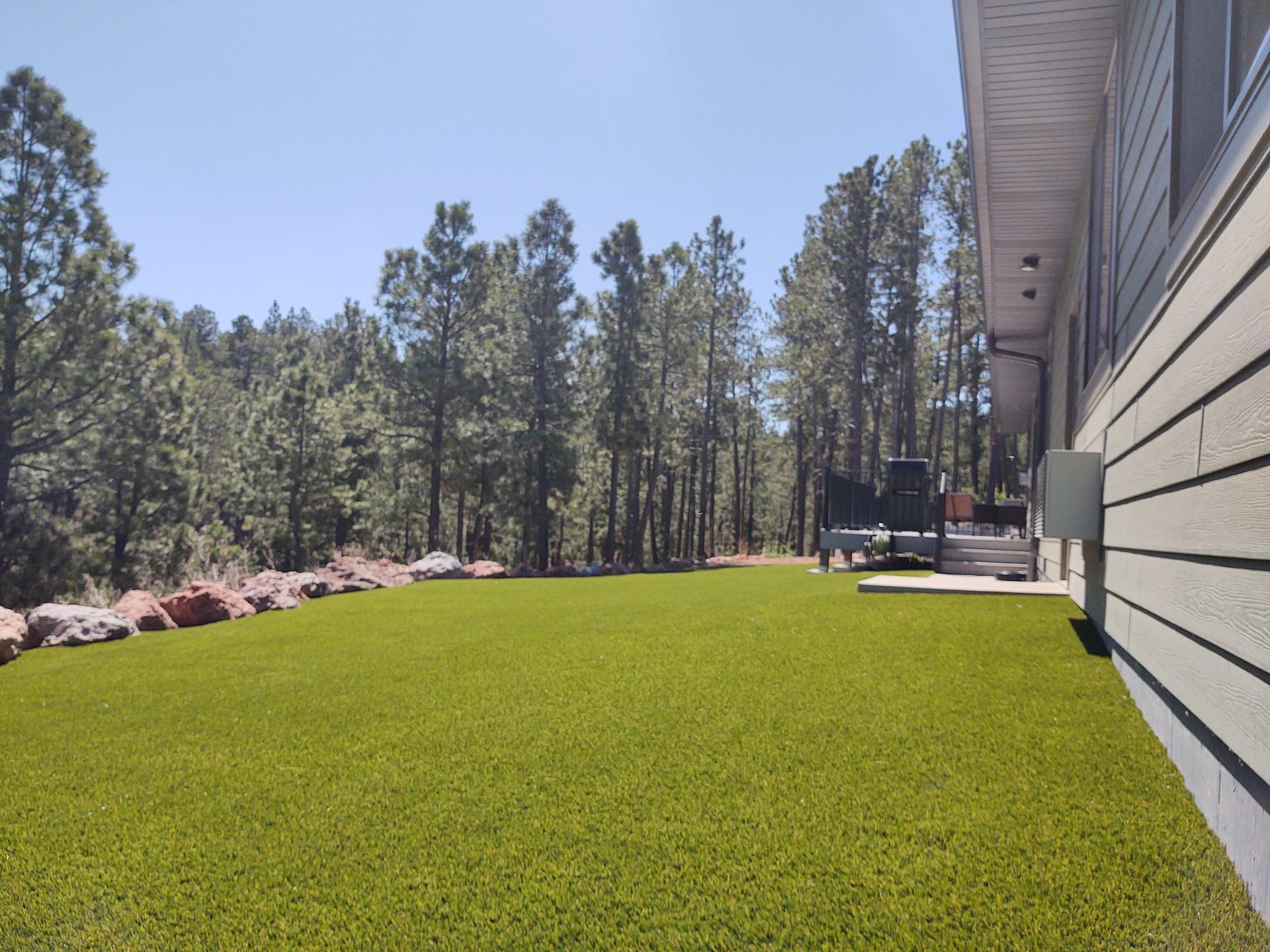 Green lawn next to a light-colored house, with trees in the background under a blue sky