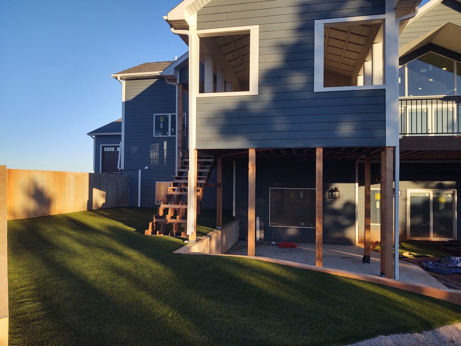 Two-story blue house with an elevated deck, staircase, and green lawn