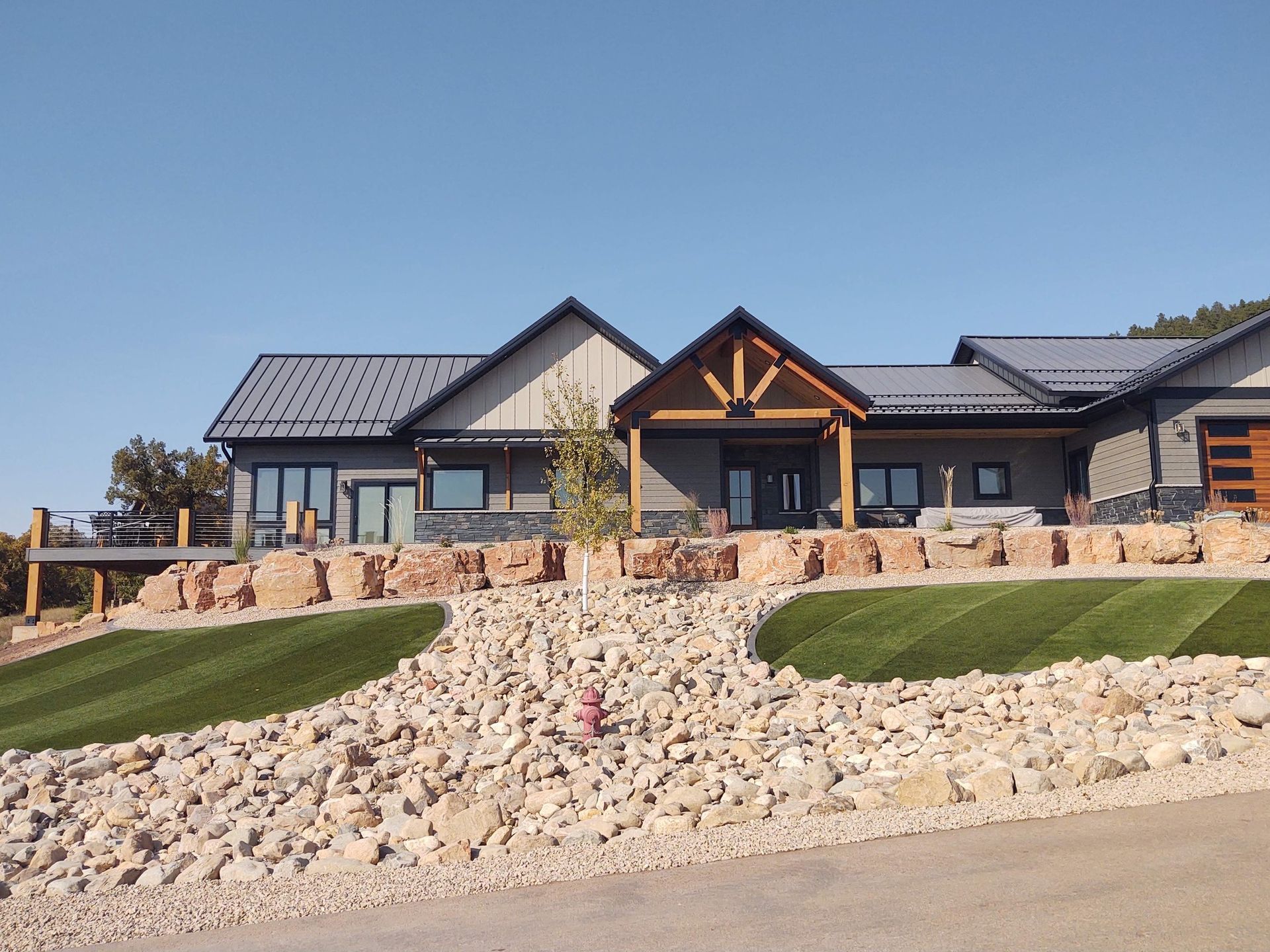 Modern house with gray siding and metal roof, built into a rocky hillside, under a blue sky