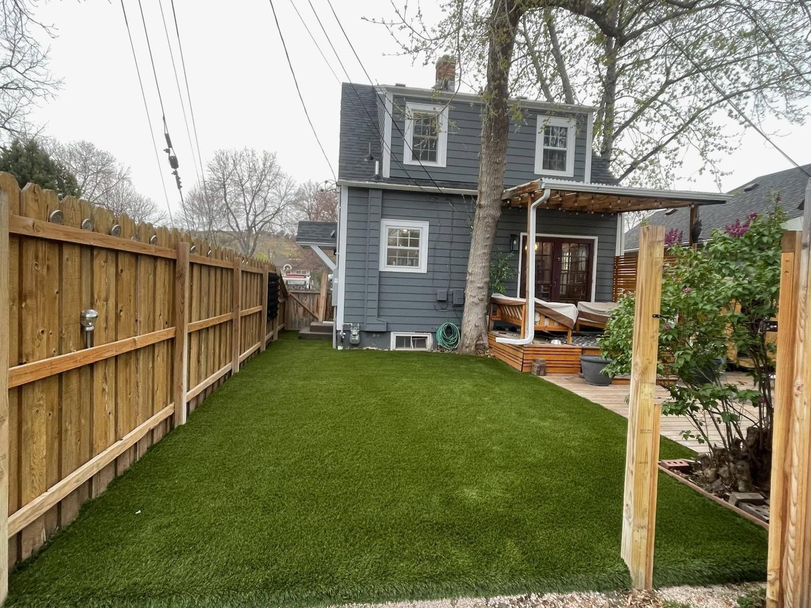 Backyard with green turf, wooden fence, gray house, and a covered porch