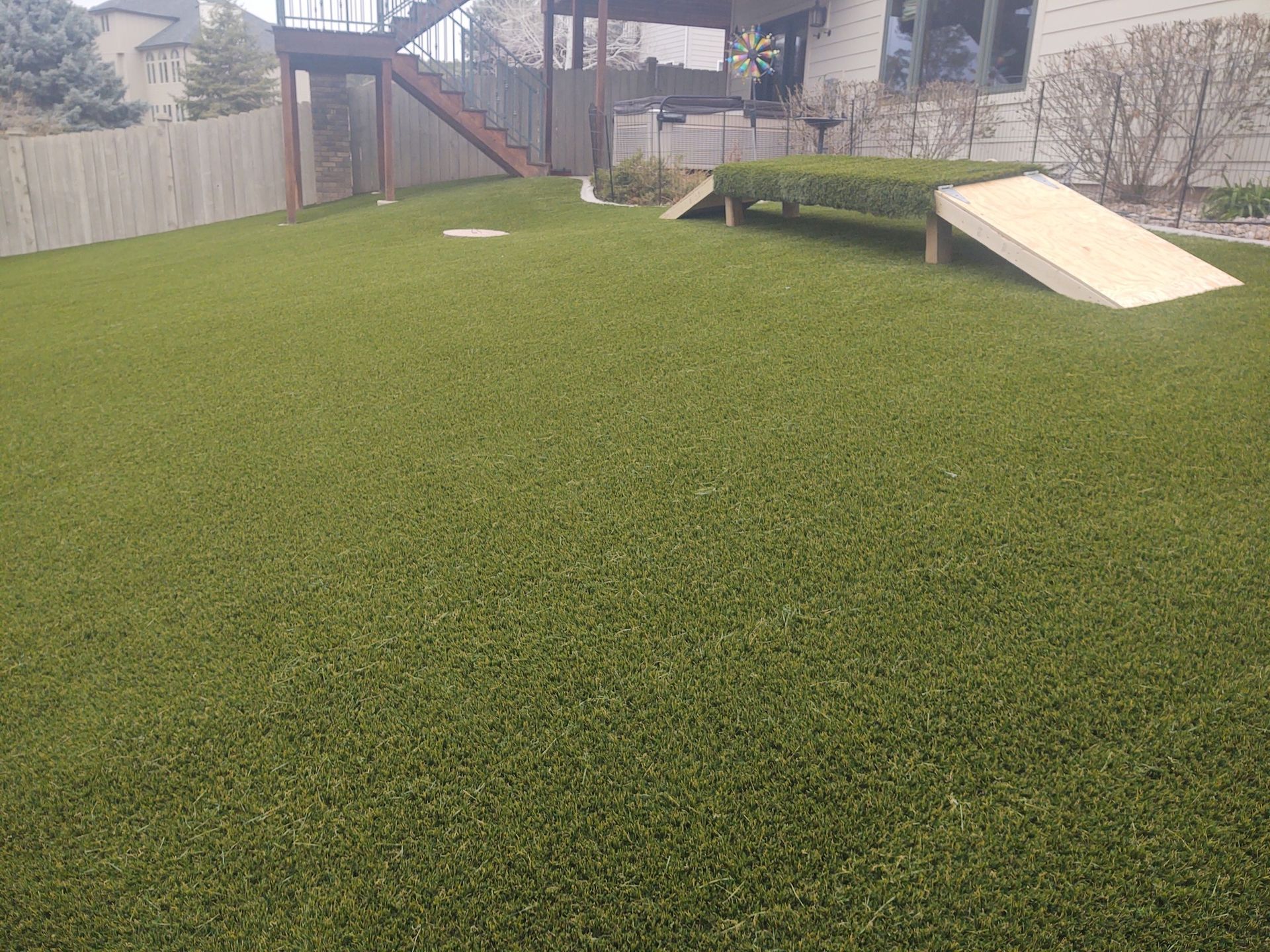 Green artificial turf backyard with wooden structures, including a ramp and cornhole game